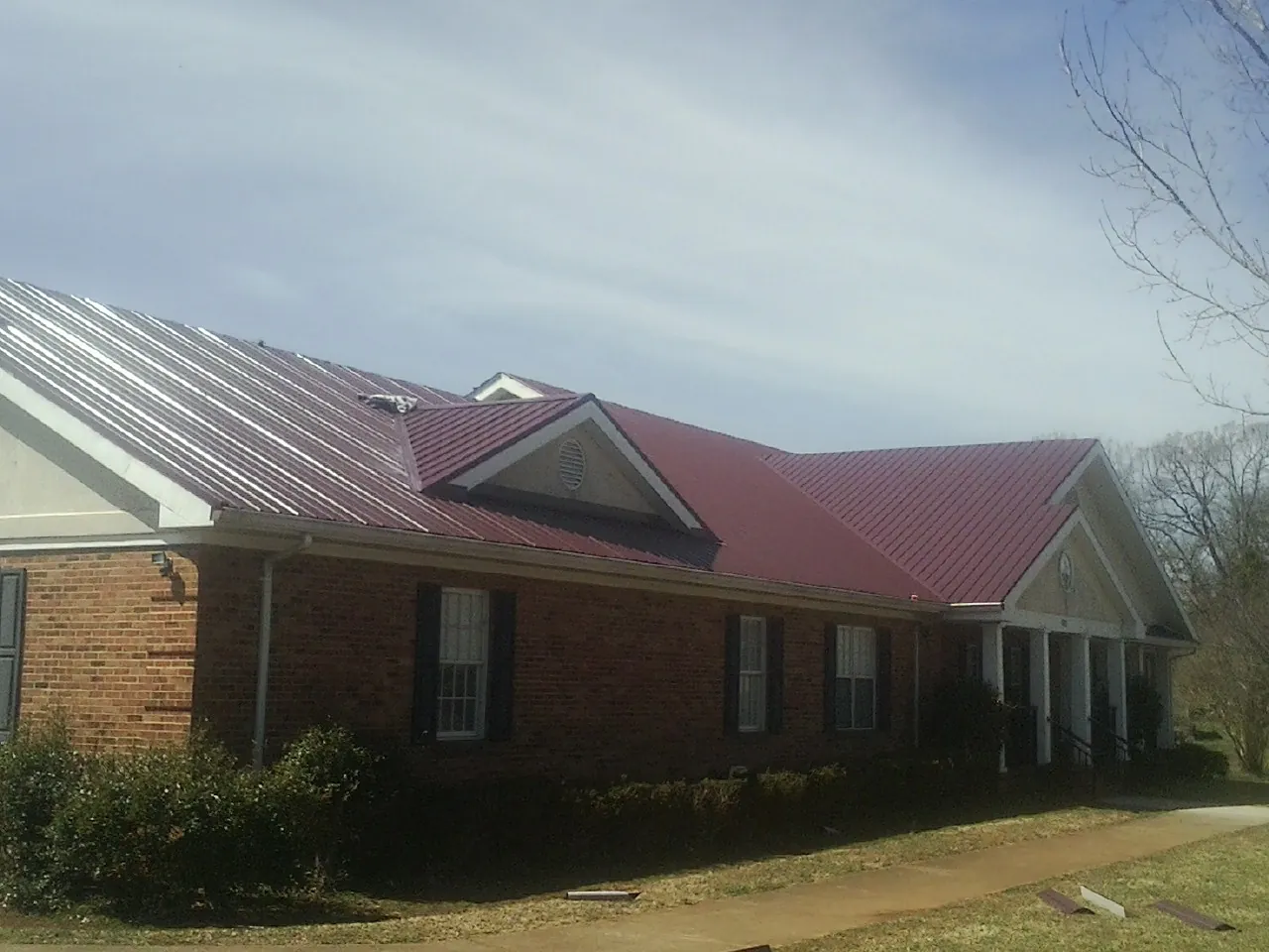 Red metal roof with gabled entries on a long brick building, from a Hail Damage Roof Repair job in Thompson Falls