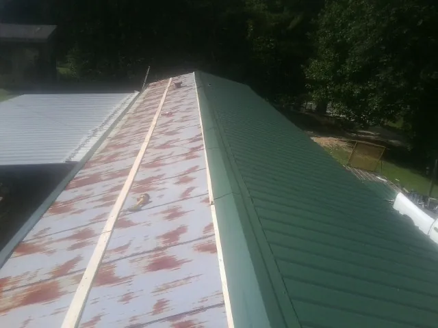 Old rusted panels beside newly installed green metal roofing — Wind Damage Roof Repair by Roofing Brothers in Thompson Falls