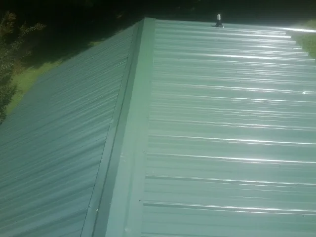 New green metal panels meeting at the ridge of a roof — Flat Roof Repair work by our crew in Thompson Falls