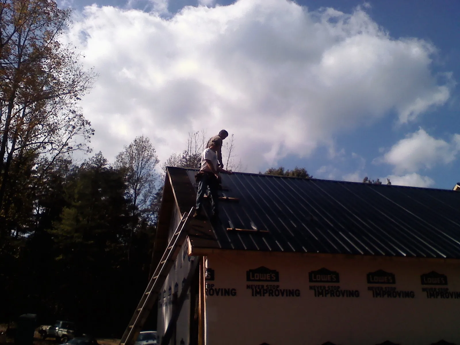 Roofer fastening dark metal panels high against a cloudy sky, from a Roof Inspection job in Thompson Falls